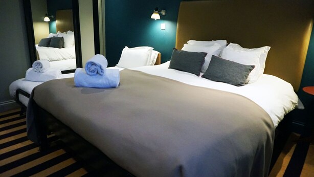 A hotel room with a large bed, a headboard, and a mirror. - The Penny Farthing (Berkhamsted)