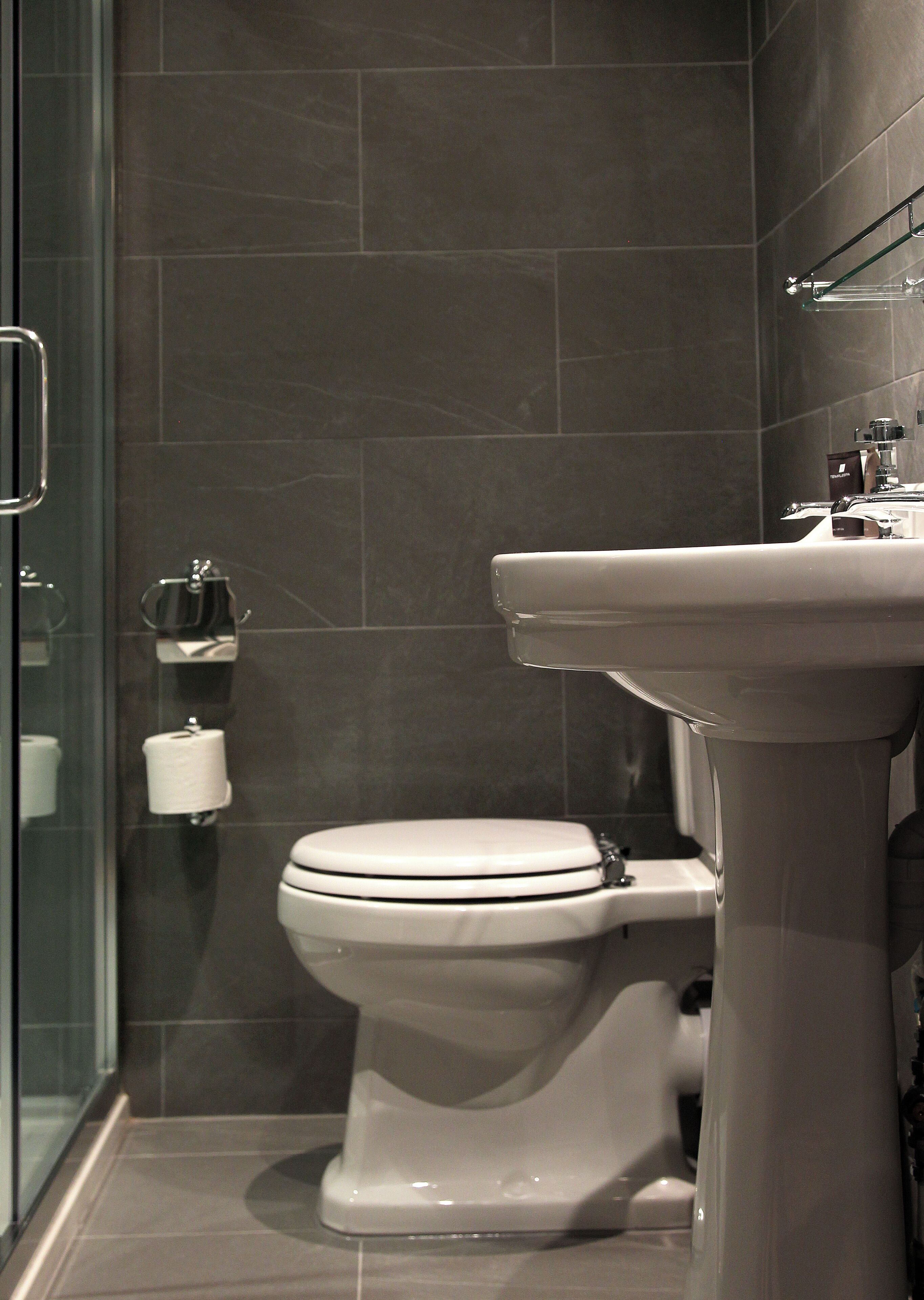 A modern bathroom with a toilet, a glass shower enclosure, and a white pedestal sink.
