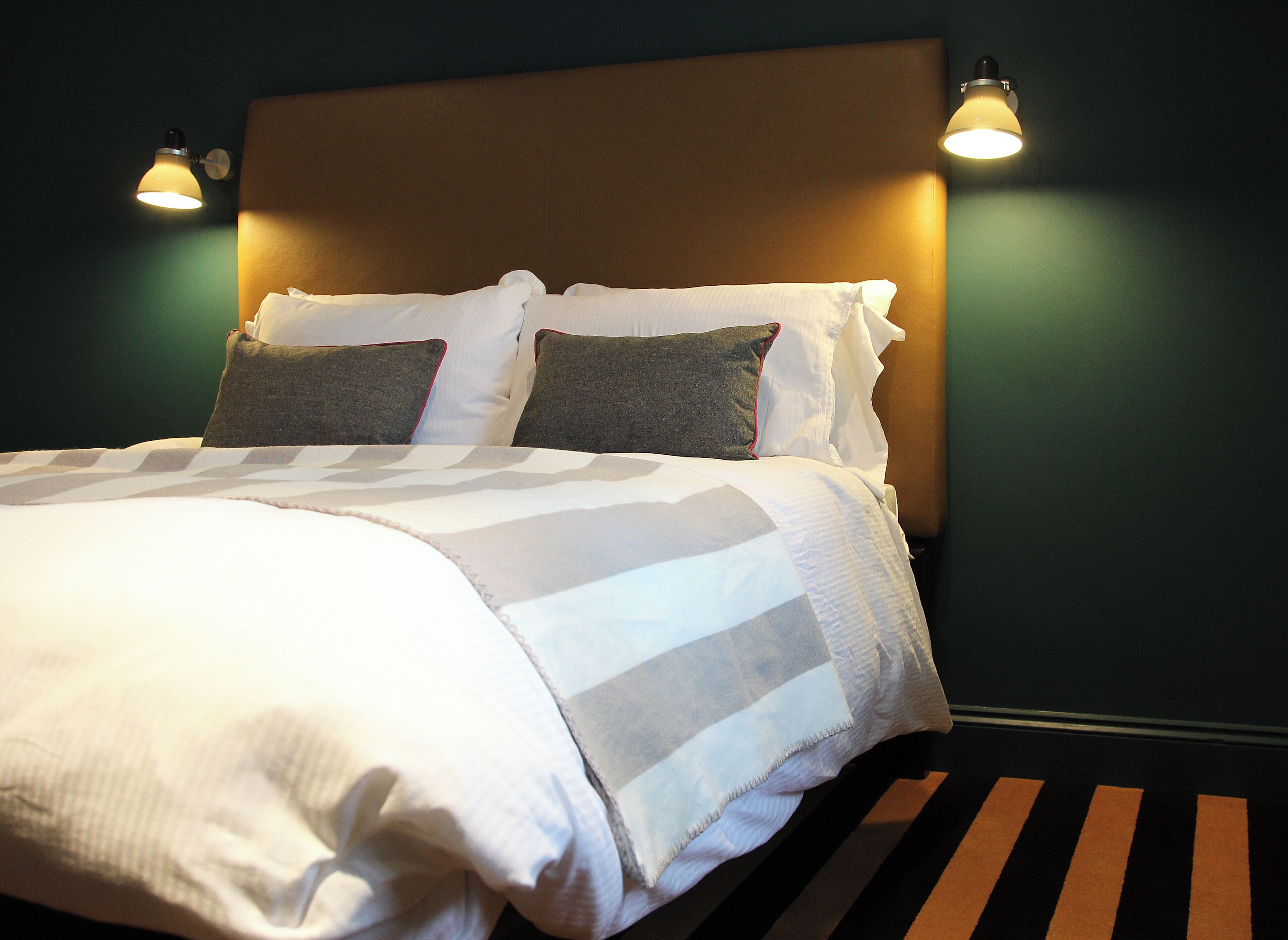 A neatly made bed with a striped bedspread and two pillows, a headboard, and two wall-mounted lamps.