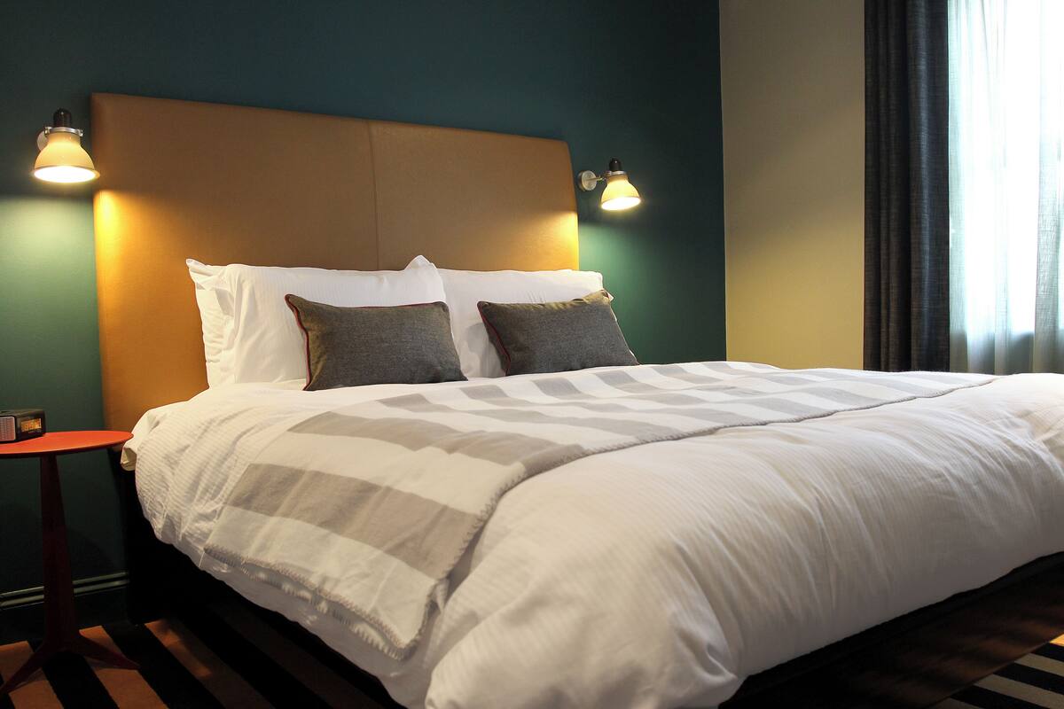 A neatly made bed with a headboard, two bedside lamps, and a striped rug.