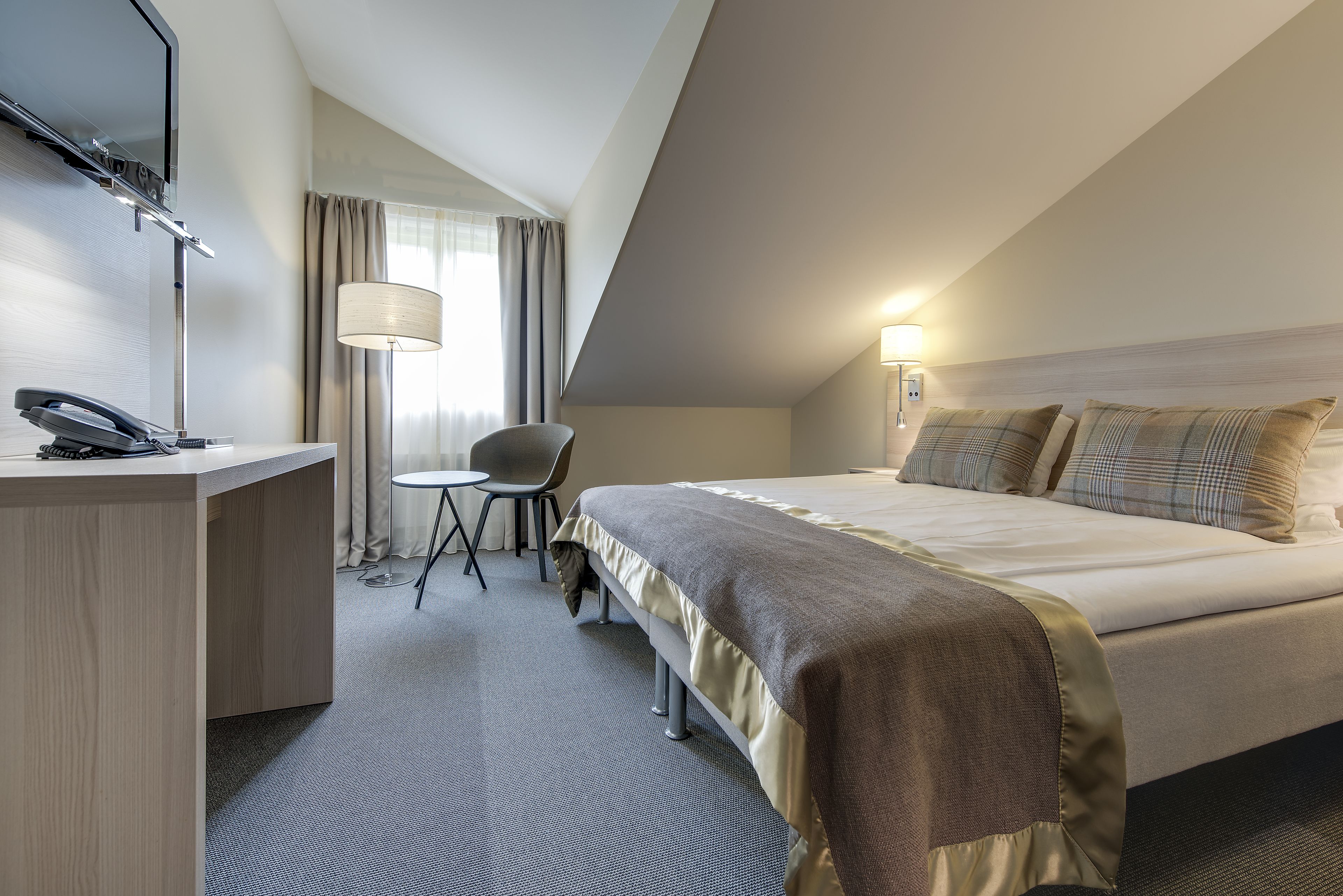 Een hotelkamer met een bed, een bureau met telefoon, een stoel en een lamp.