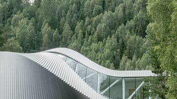 Una estructura arquitectónica moderna con techo curvo, rodeada por un paisaje boscoso.