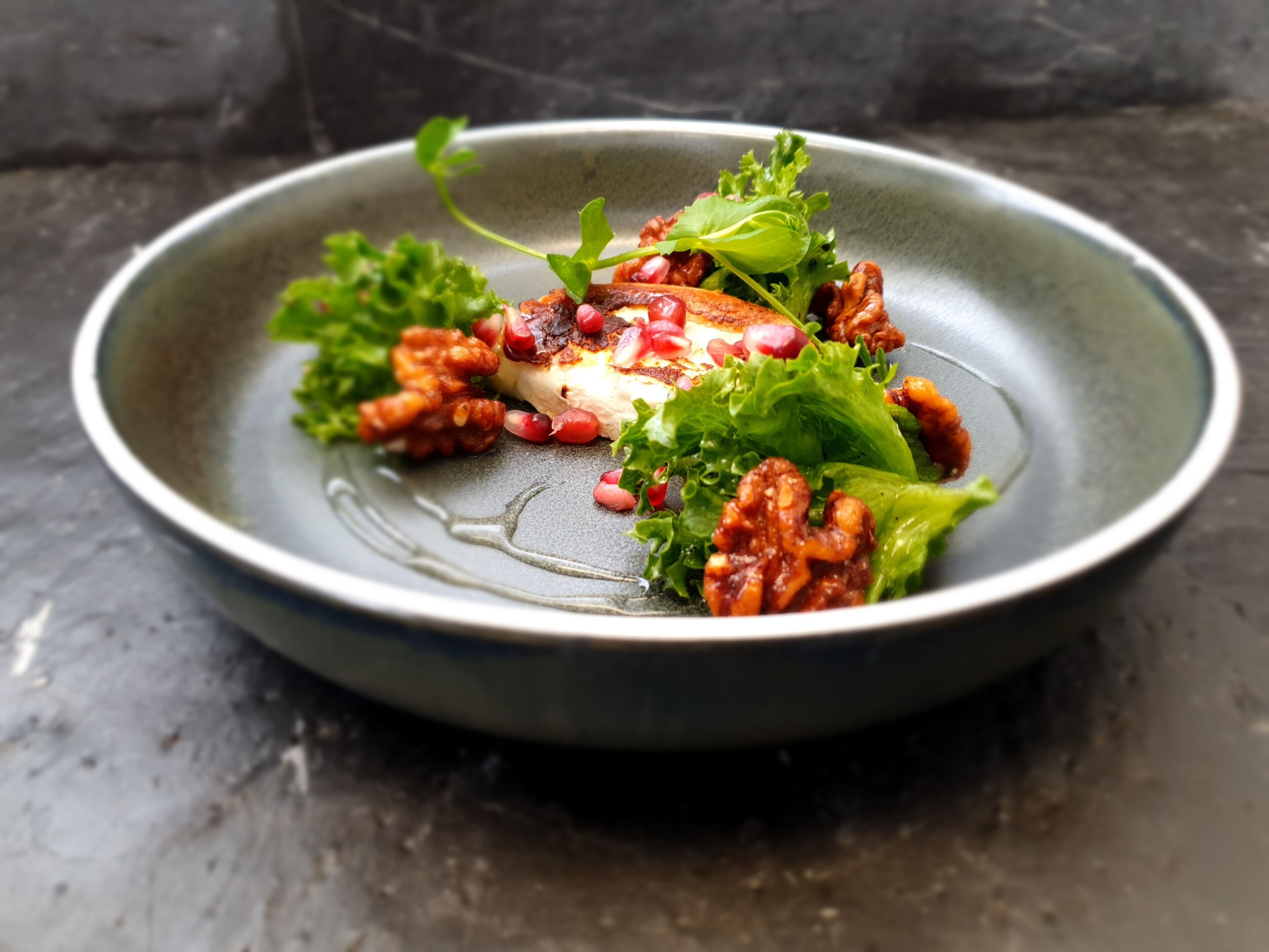 A plate of food with greens, nuts, and pomegranate seeds.