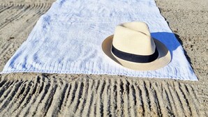A beach scene with a towel and a hat on the sand, a boat in the water, and a distant shoreline. - Tyrifjord Hotell (Modum)