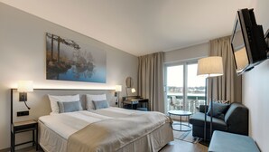A hotel room with a large bed, a sofa, a small table, a TV, and a painting on the wall. - Tyrifjord Hotell (Modum)