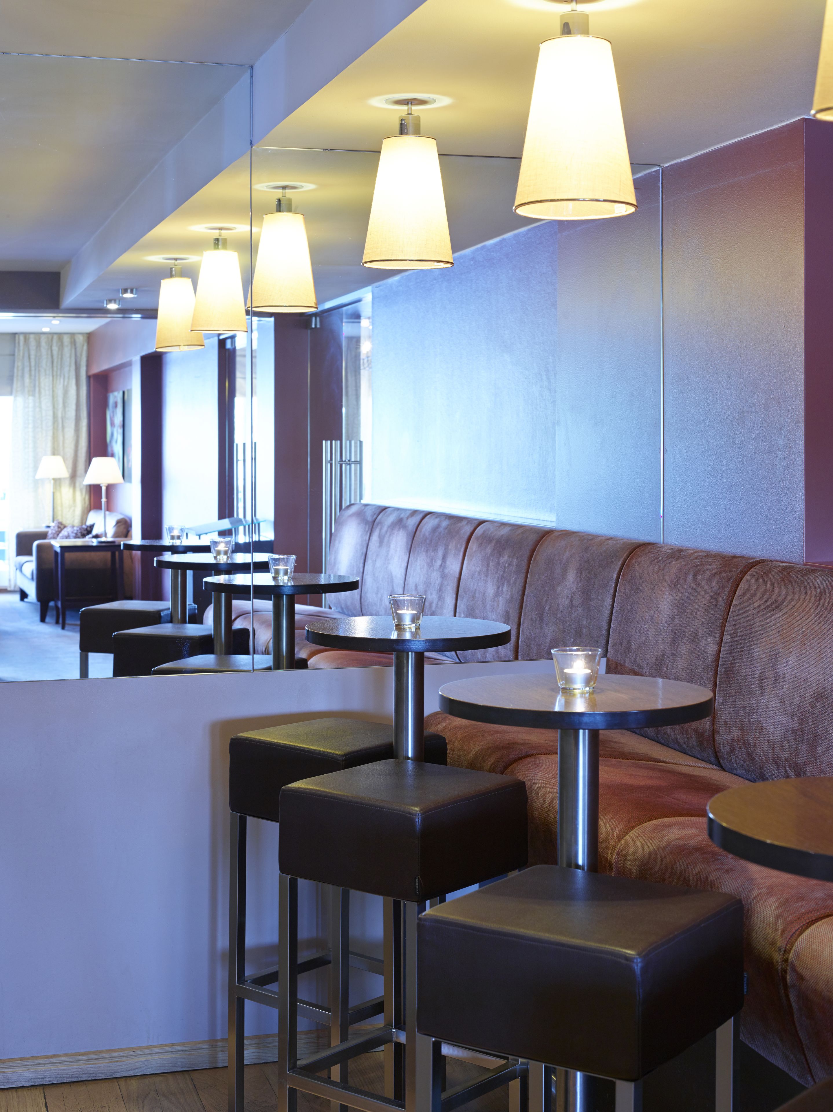 A modern restaurant with booth seating and round tables, featuring pendant lighting and a neutral color palette.
