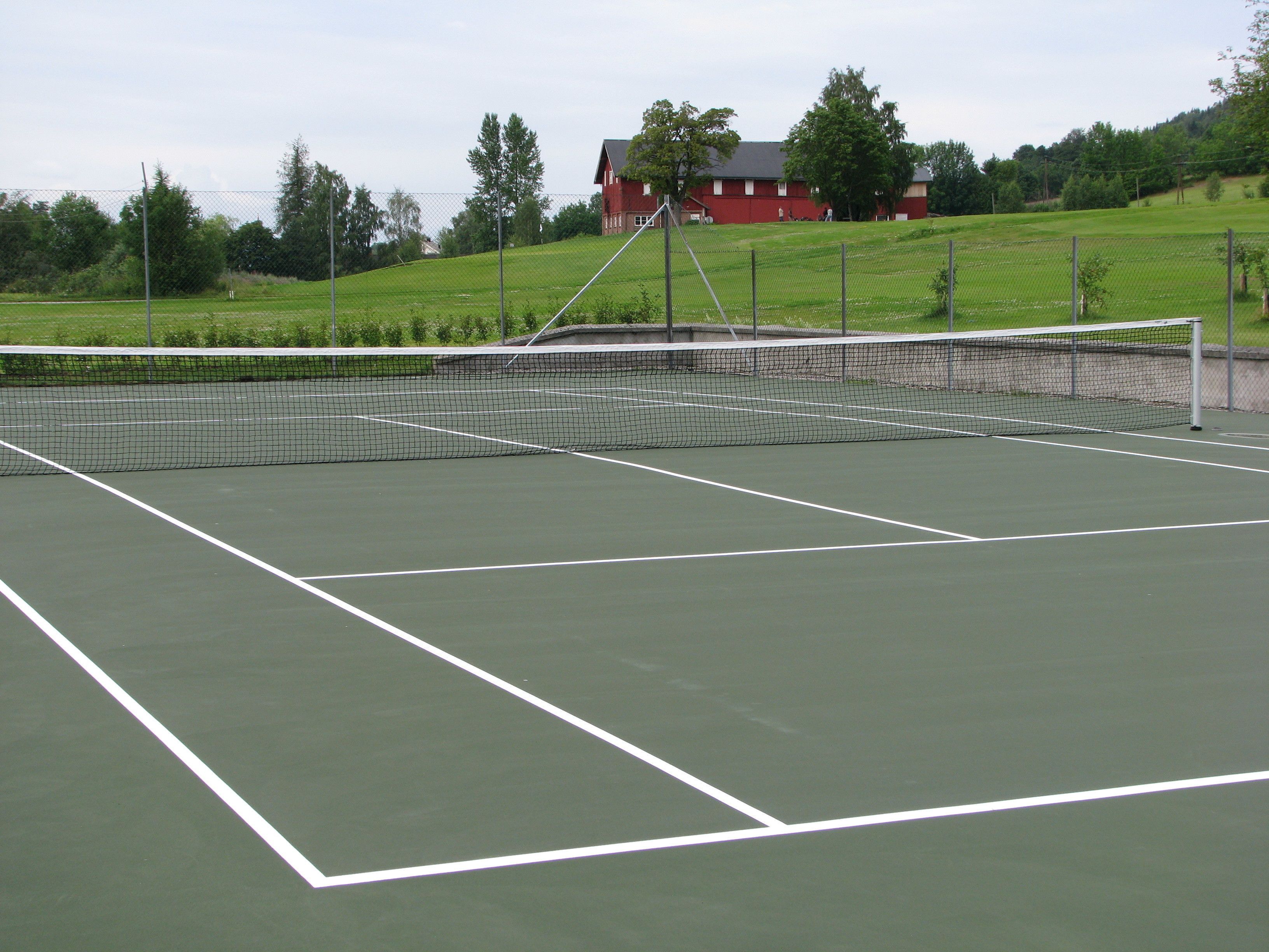 A tennis court with a net, surrounded by a fence and trees.