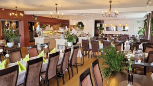 A spacious dining area with multiple tables and chairs, a central counter, and decorative plants. - Tyrifjord Hotell (Modum)