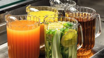 Diversas bebidas em jarras de vidro e canecas, algumas com gelo e guarnições, sobre uma superfície metálica.
