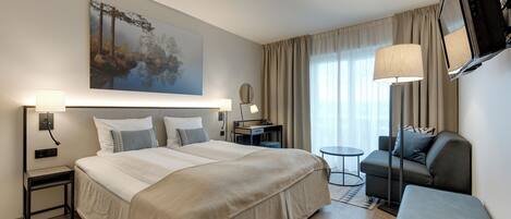 A hotel room with a large bed, a desk, a sofa, a TV, and a painting on the wall.