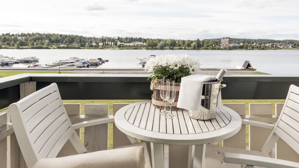 A round table with chairs on an outdoor deck, overlooking a lake with boats and houses in the distance. - Tyrifjord Hotell (Modum)
