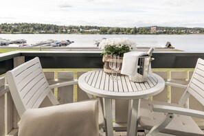 A round table with chairs on an outdoor deck, overlooking a lake with boats and houses in the distance. - Tyrifjord Hotell (Modum)