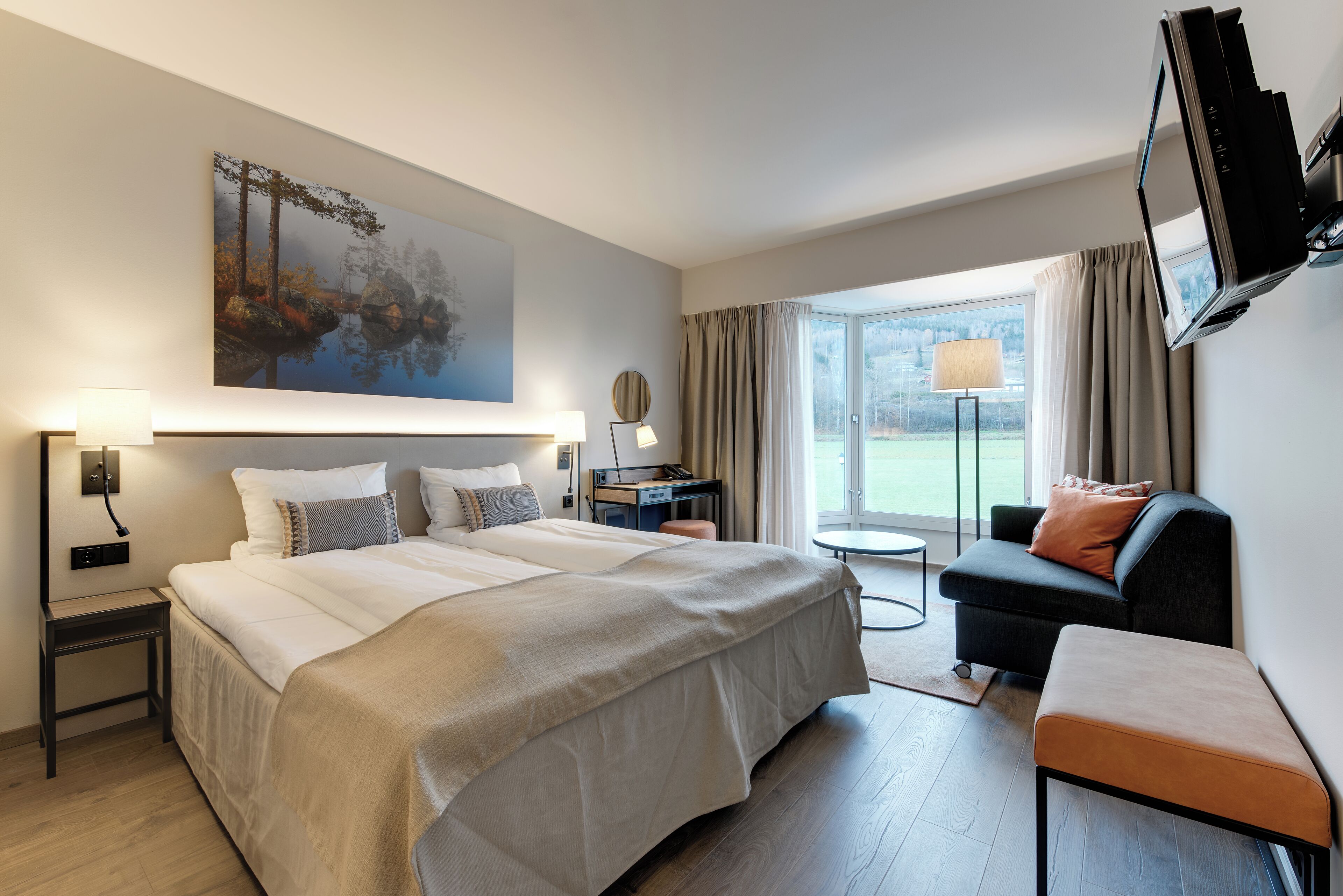 A hotel room with a large bed, a desk, a chair, a TV, and a window with a view.