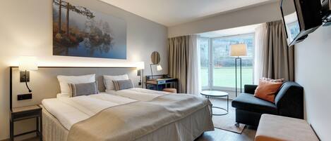 A hotel room with a large bed, a desk, a chair, a TV, and a window with a view.