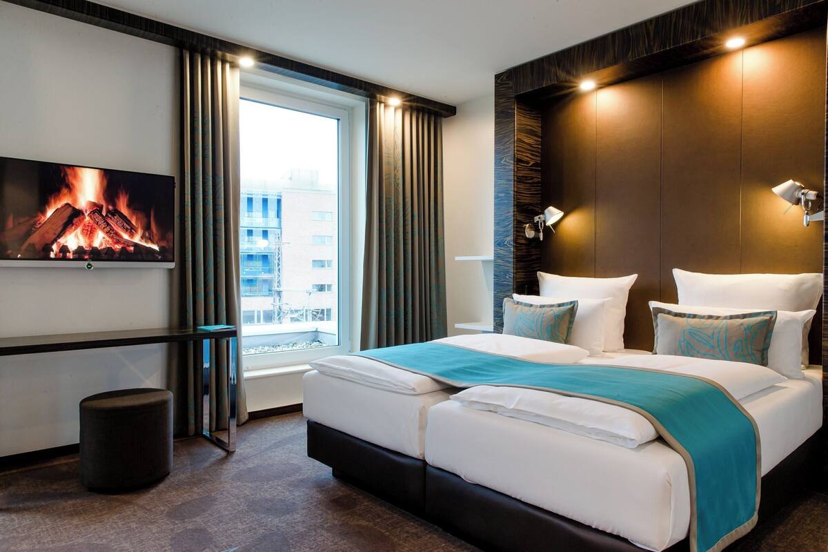 A hotel room with a large bed, a TV mounted on the wall, and a window with curtains.