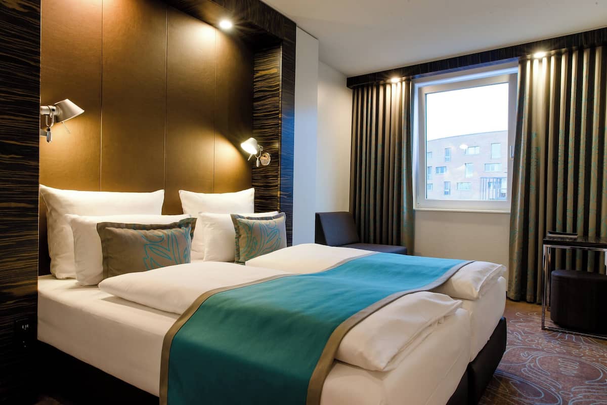 Quarto de hotel com uma cama grande, uma escrivaninha e uma janela com cortinas.