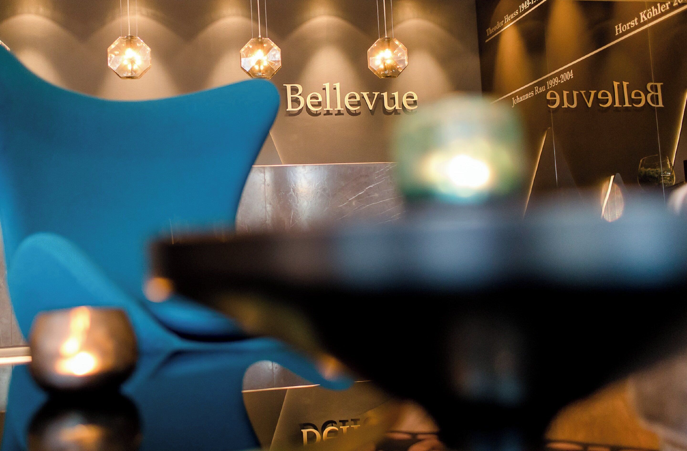 L’intérieur d’un hôtel, avec une enseigne « Bellevue » bien visible, un fauteuil bleu et des luminaires suspendus.