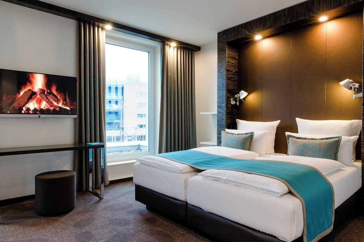A hotel room with a large bed, a TV mounted on the wall, and a window with curtains.
