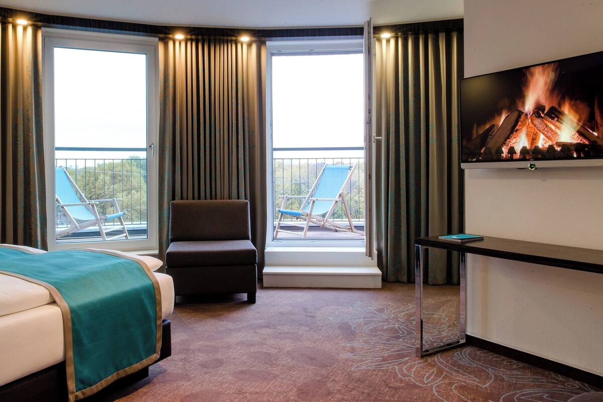 A hotel room with a bed, a chair, a TV, and a balcony with a view.