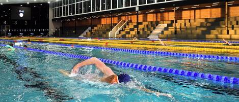 An indoor swimming pool with lane dividers and a digital clock displaying 15:45.