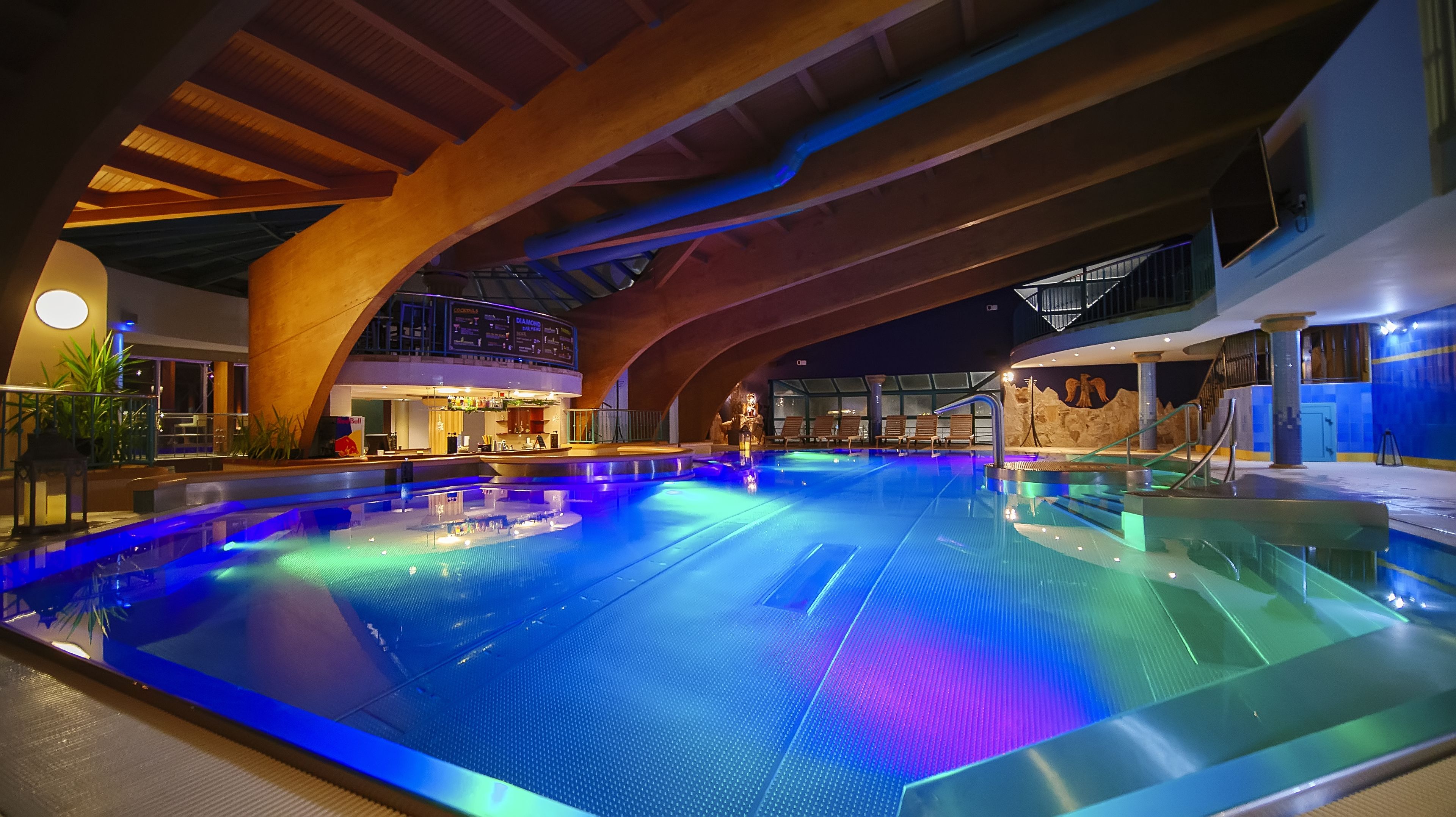 Una amplia piscina cubierta con diseño moderno, que cuenta con un techo alto y un elemento acuático central.