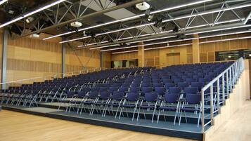 An auditorium with rows of blue chairs, a stage, and a wooden floor.