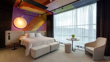 Une chambre d’hôtel moderne avec un grand lit, un canapé, une petite table avec une plante et une chaise.