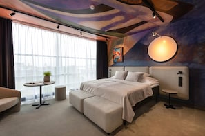 Ein modernes Hotelzimmer mit einem großen Bett, einem kleinen runden Tisch, einer Couch und einem großen Fenster mit Vorhängen.