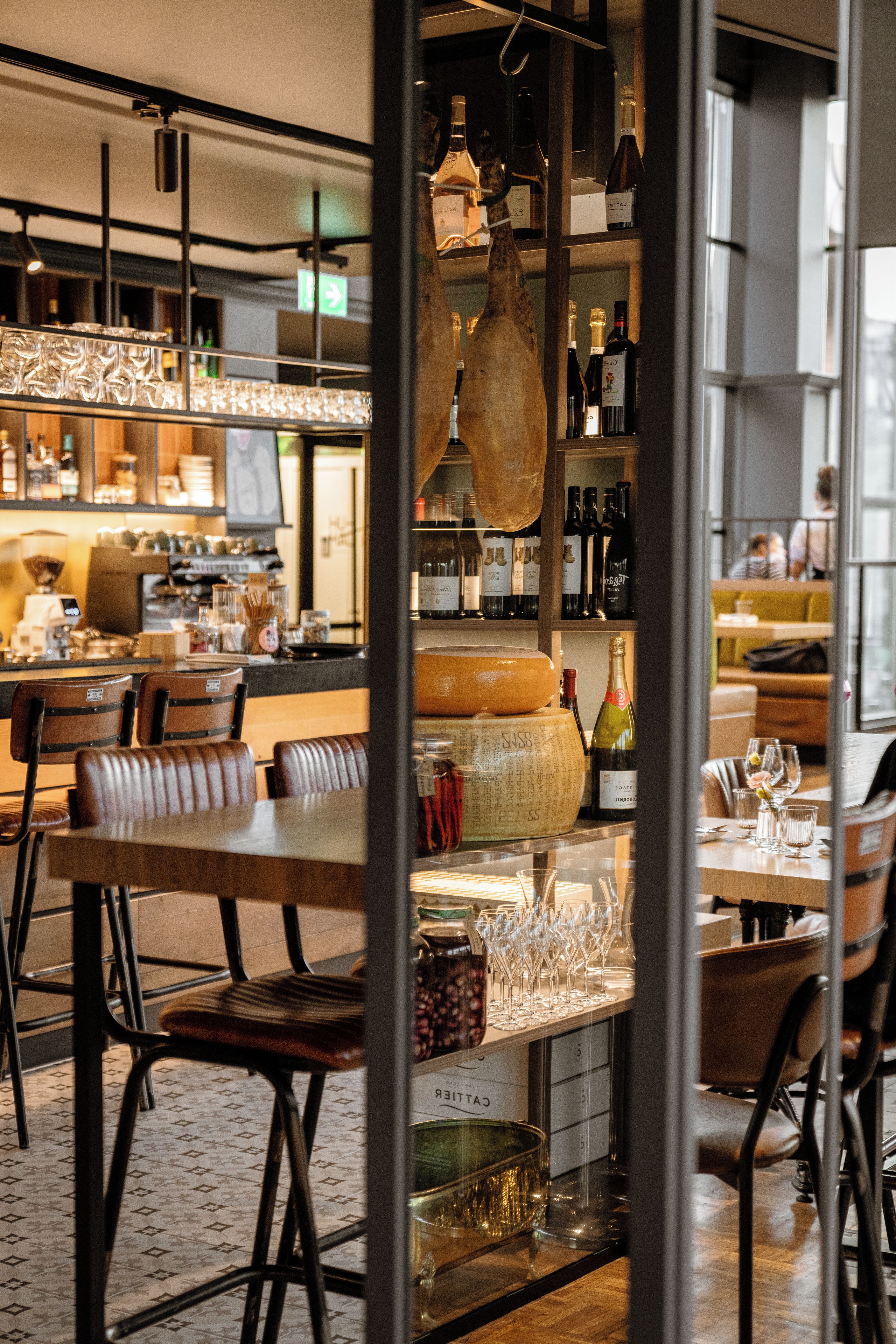 Un interior de restaurante con barra, mesas y sillas, y una estantería para vinos.