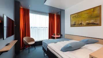 A hotel room with a bed, a chair, a desk, a TV, and a painting on the wall.