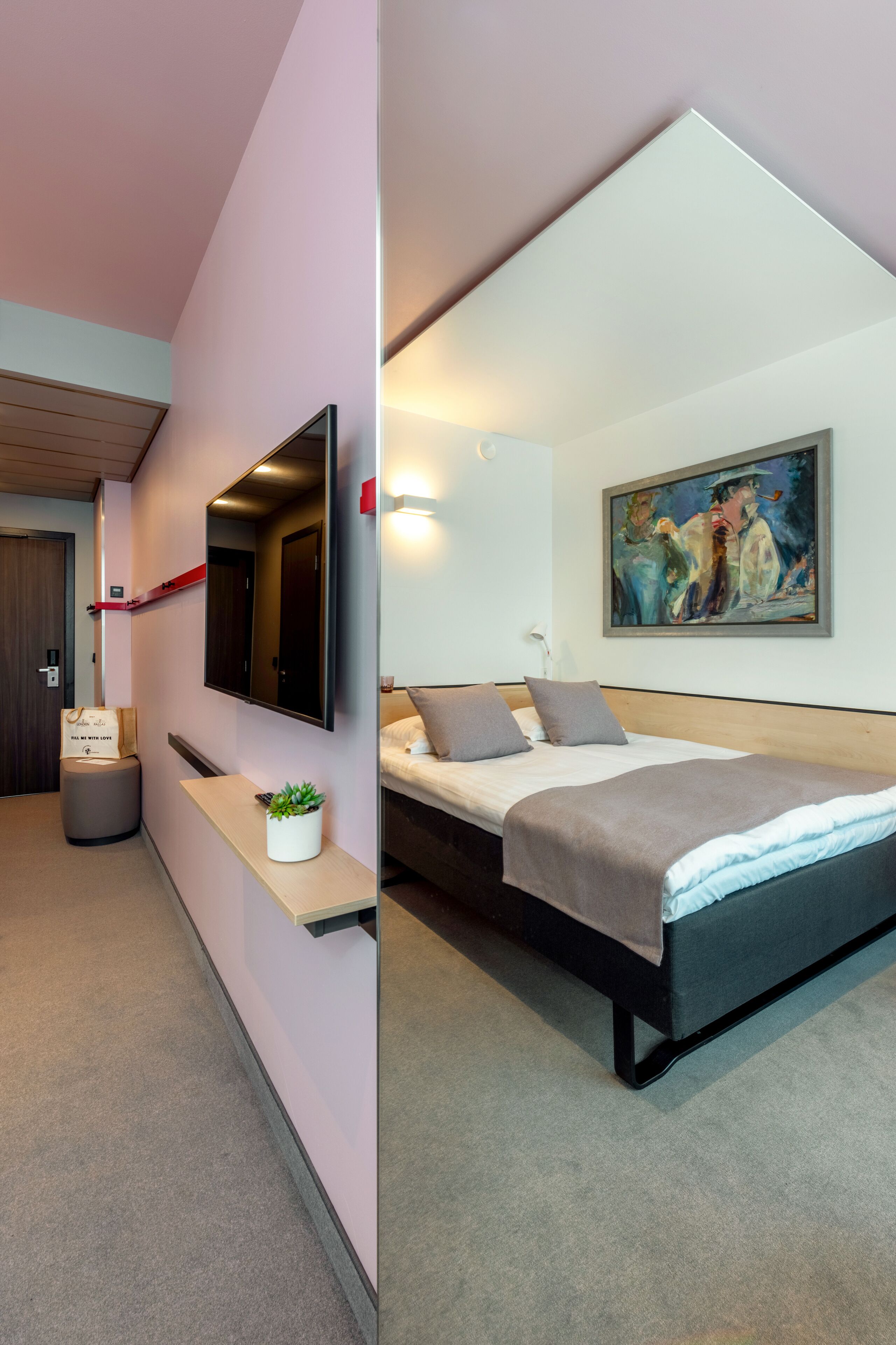 A modern hotel room with a bed, a mounted TV, a painting on the wall, and a small plant on a bedside table.