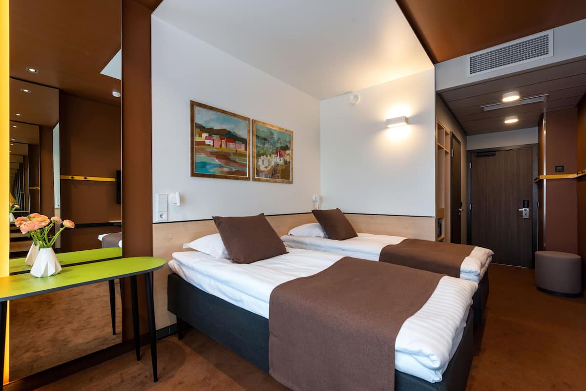 Ein Hotelzimmer mit zwei Betten, einem Schreibtisch mit Blumenvase und einem Bild an der Wand.
