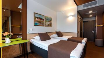 A hotel room with two beds, a desk with a vase of flowers, and a painting on the wall.