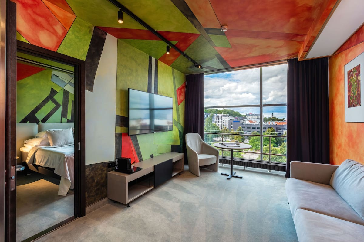 Ein modernes Hotelzimmer mit Bett, Fernseher, Sofa und Balkon mit Blick auf die Stadt.