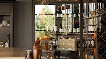 A modern bar area with a variety of wine bottles and glasses on shelves, a wooden table, and a view of the outdoors.