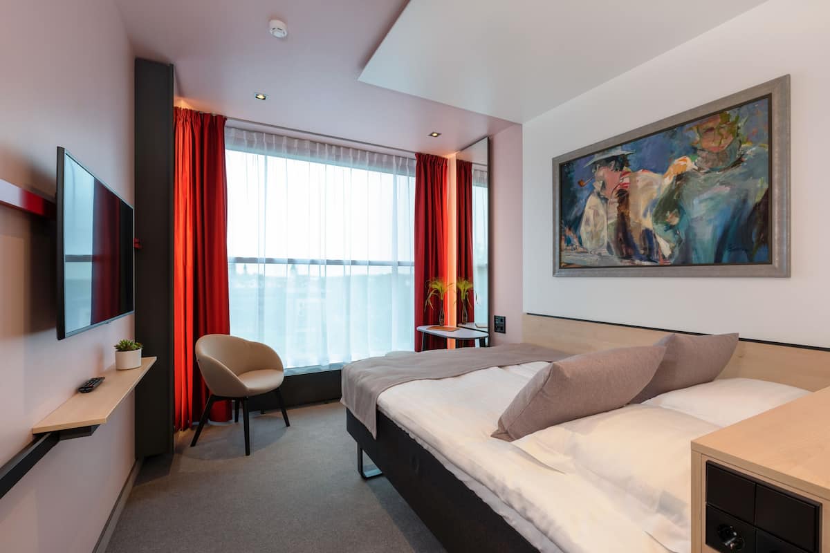 Ein modernes Hotelzimmer mit Bett, Sessel, Schreibtisch, Fernseher und einem Gemälde an der Wand.