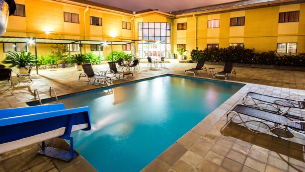 Piscina interior con sillas de descanso y mesas, rodeada de paredes amarillas y plantas en macetas.