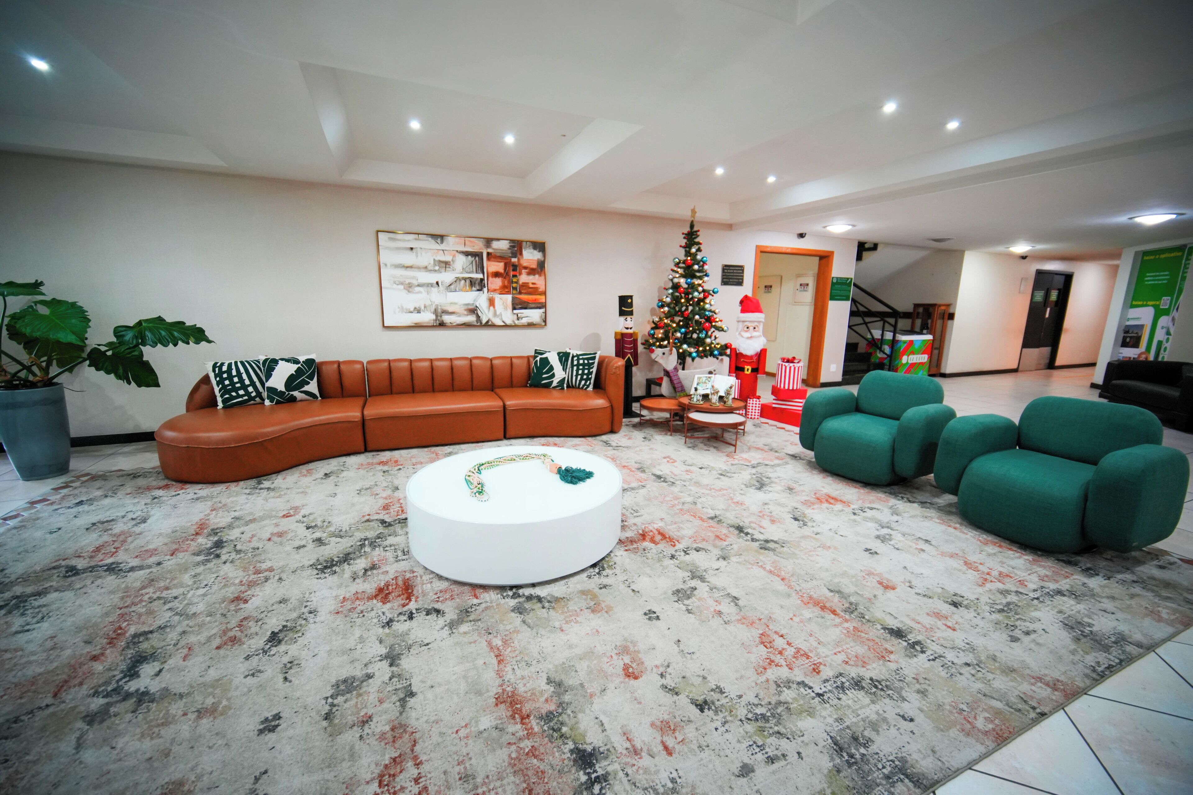 A modern living room with a curved sofa, a round coffee table, and green armchairs. A Christmas tree and a Santa Claus figure are visible in the background.