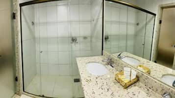 A bathroom with a glass-enclosed shower, a sink with a mirror, and a countertop with toiletries.