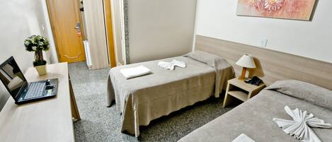 Habitación de hotel con dos camas, un escritorio con una computadora portátil, una mesita con una lámpara y un cuadro en la pared.