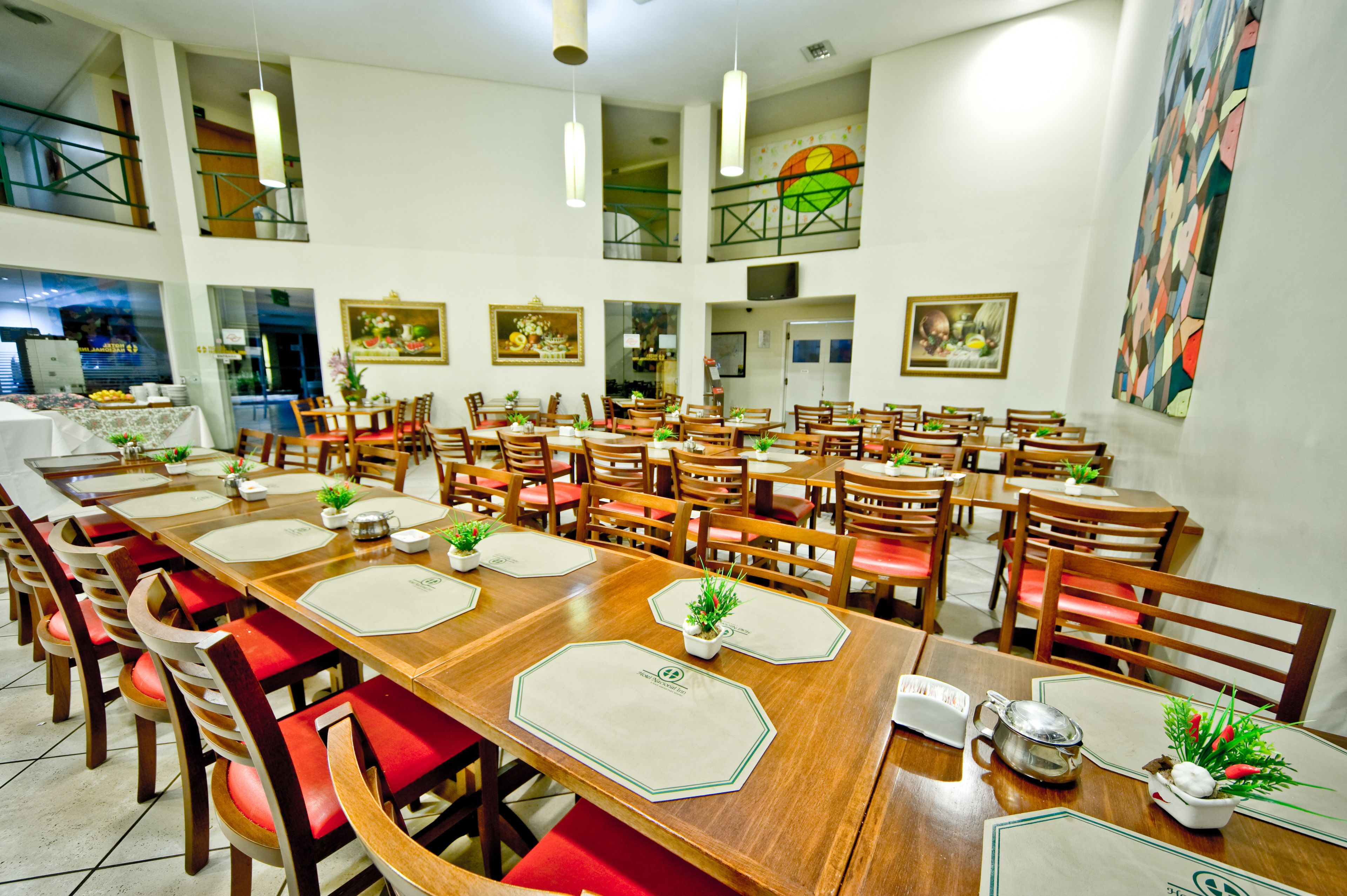 A spacious dining area with multiple tables and chairs, large windows, and artwork on the walls.