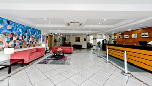 Un vestíbulo de hotel con un mostrador de recepción, un sofá rojo, una mesa de centro y un mural abstracto colorido en la pared.