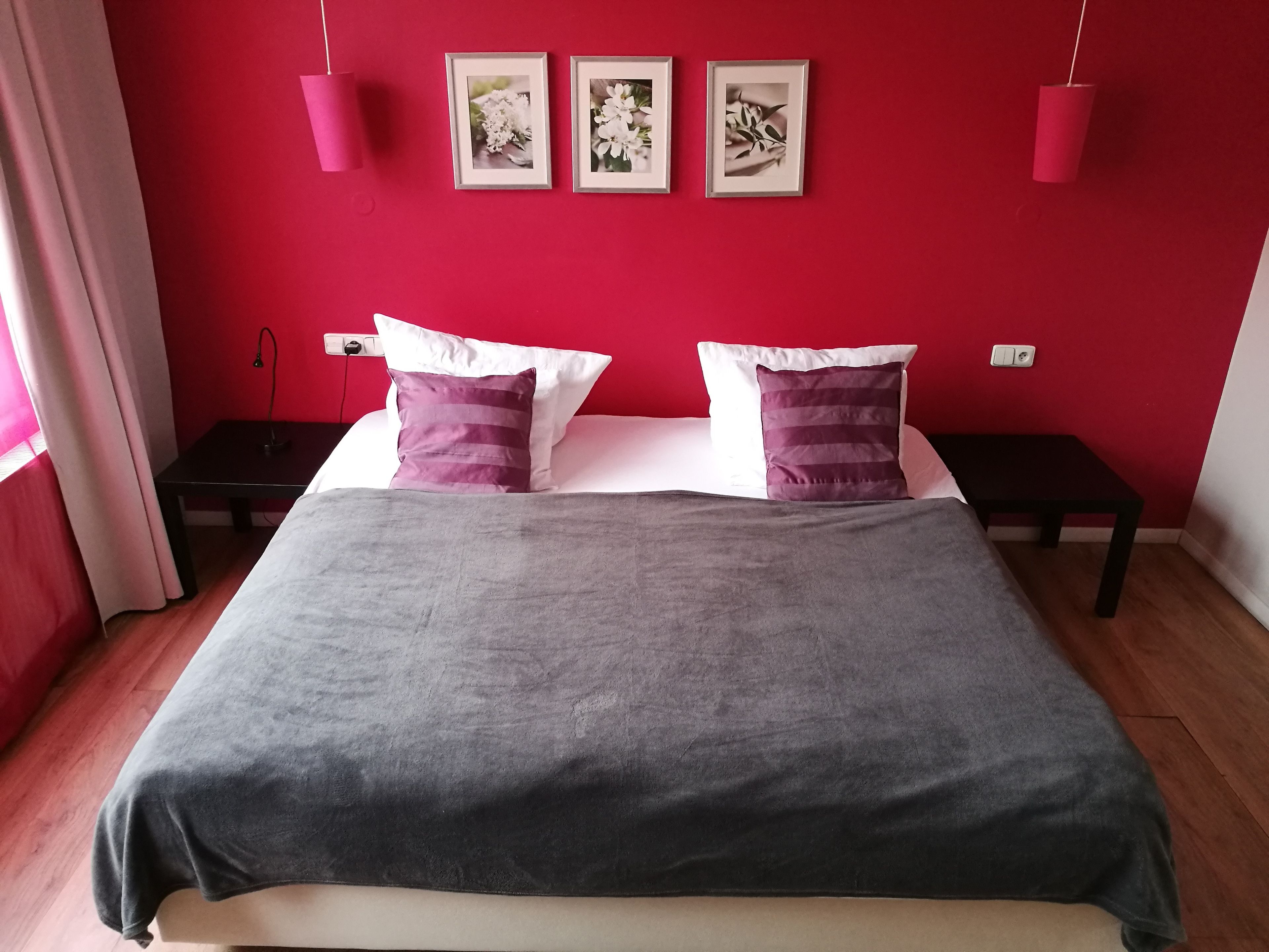 A bedroom with a bed, two nightstands, a red wall, and three framed pictures.
