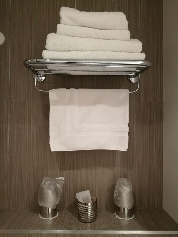 A bathroom with a towel rack holding three folded towels and a single towel hanging below. There are two metallic dispensers on the floor, one of which contains a tissue.