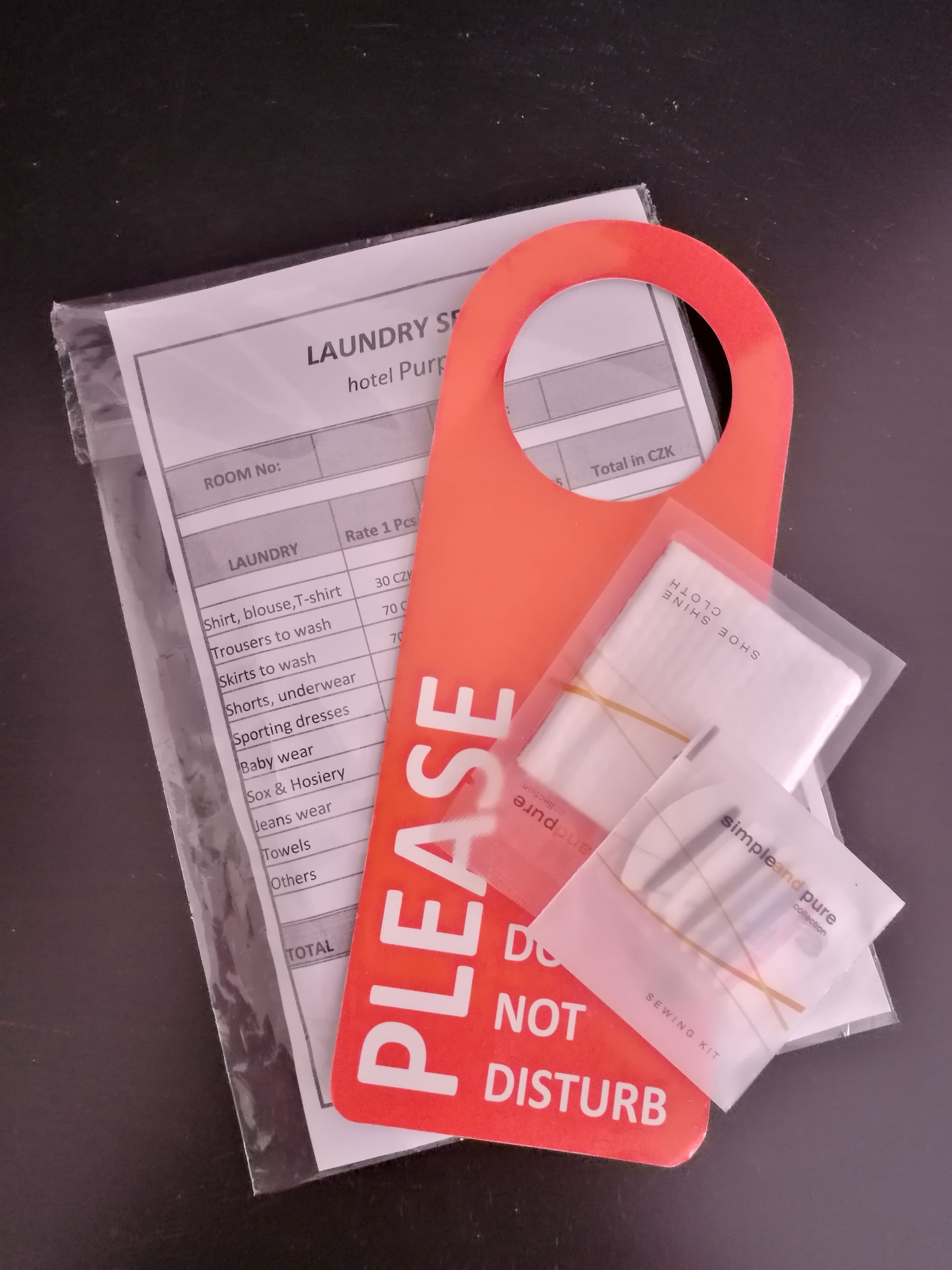 A hotel laundry service sign with a red 'PLEASE DO NOT DISTURB' sign and a small sewing kit.