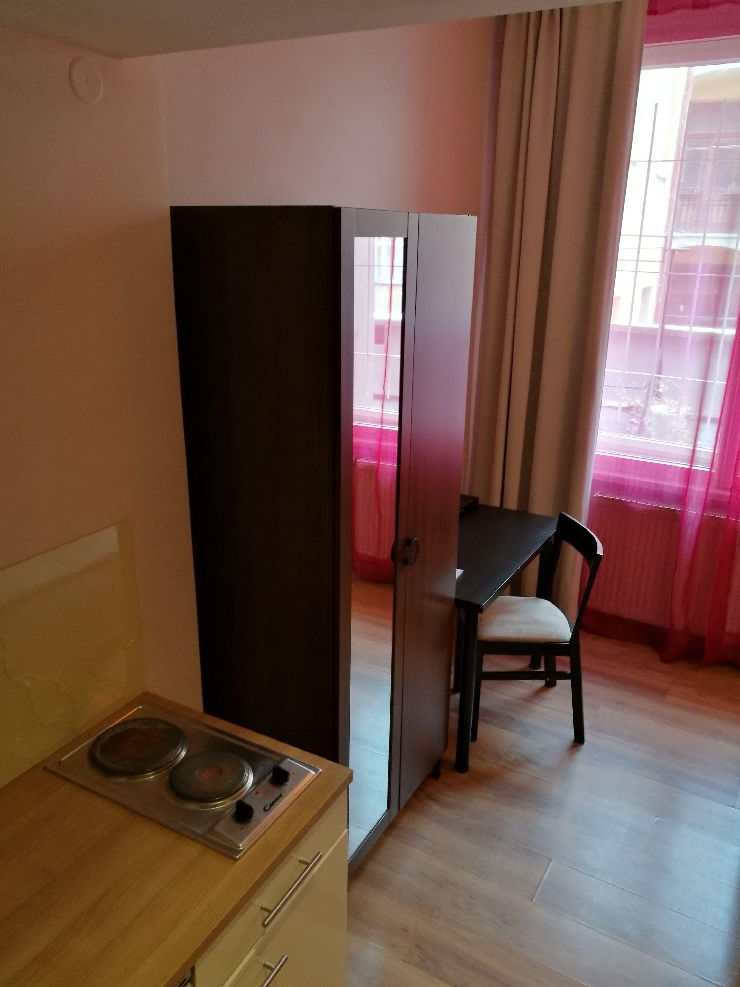 A compact kitchen with a stove, a dining table with a chair, and a wardrobe.