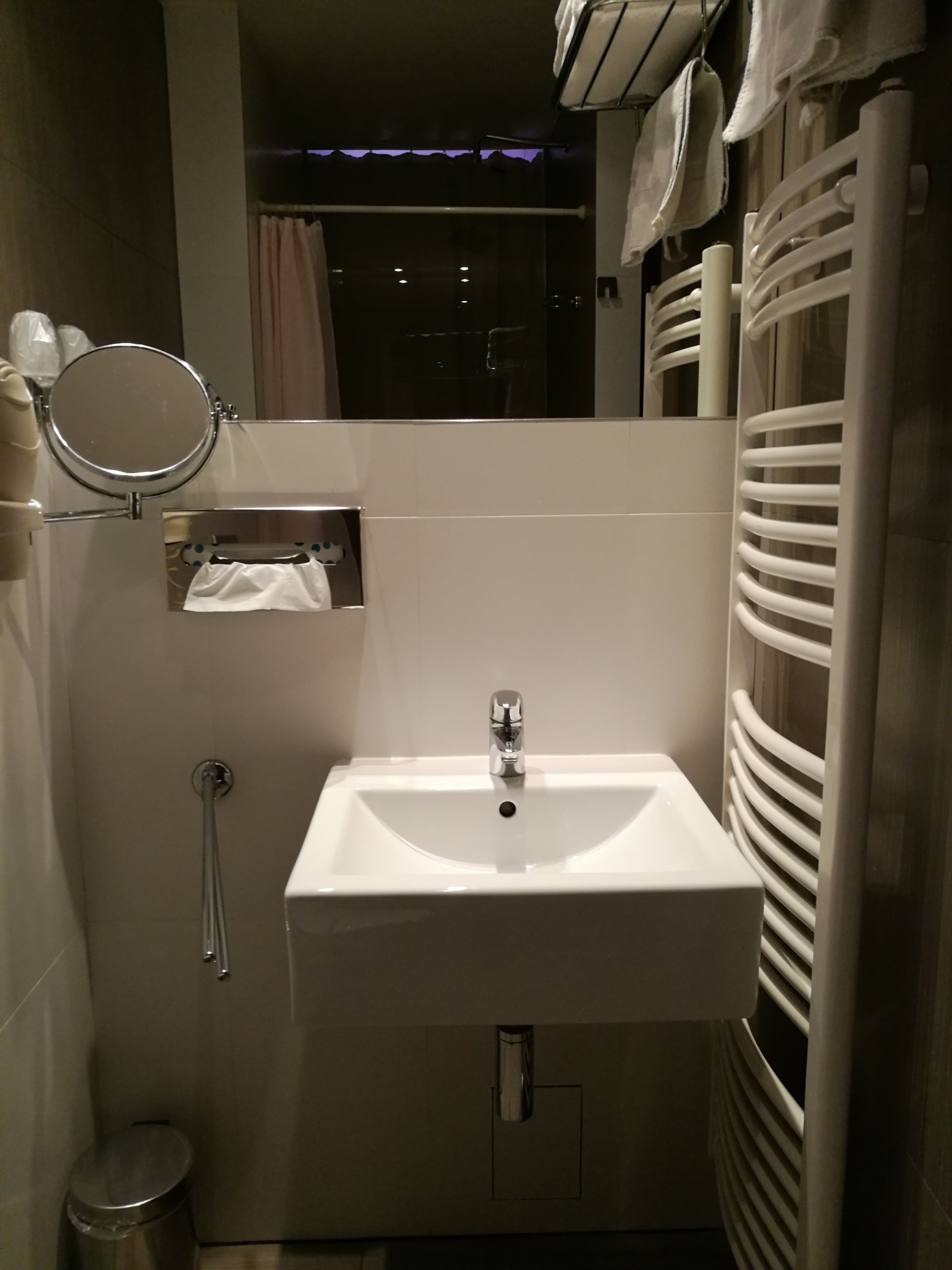Un baño con lavamanos blanco, un espejo, toallero y ducha.