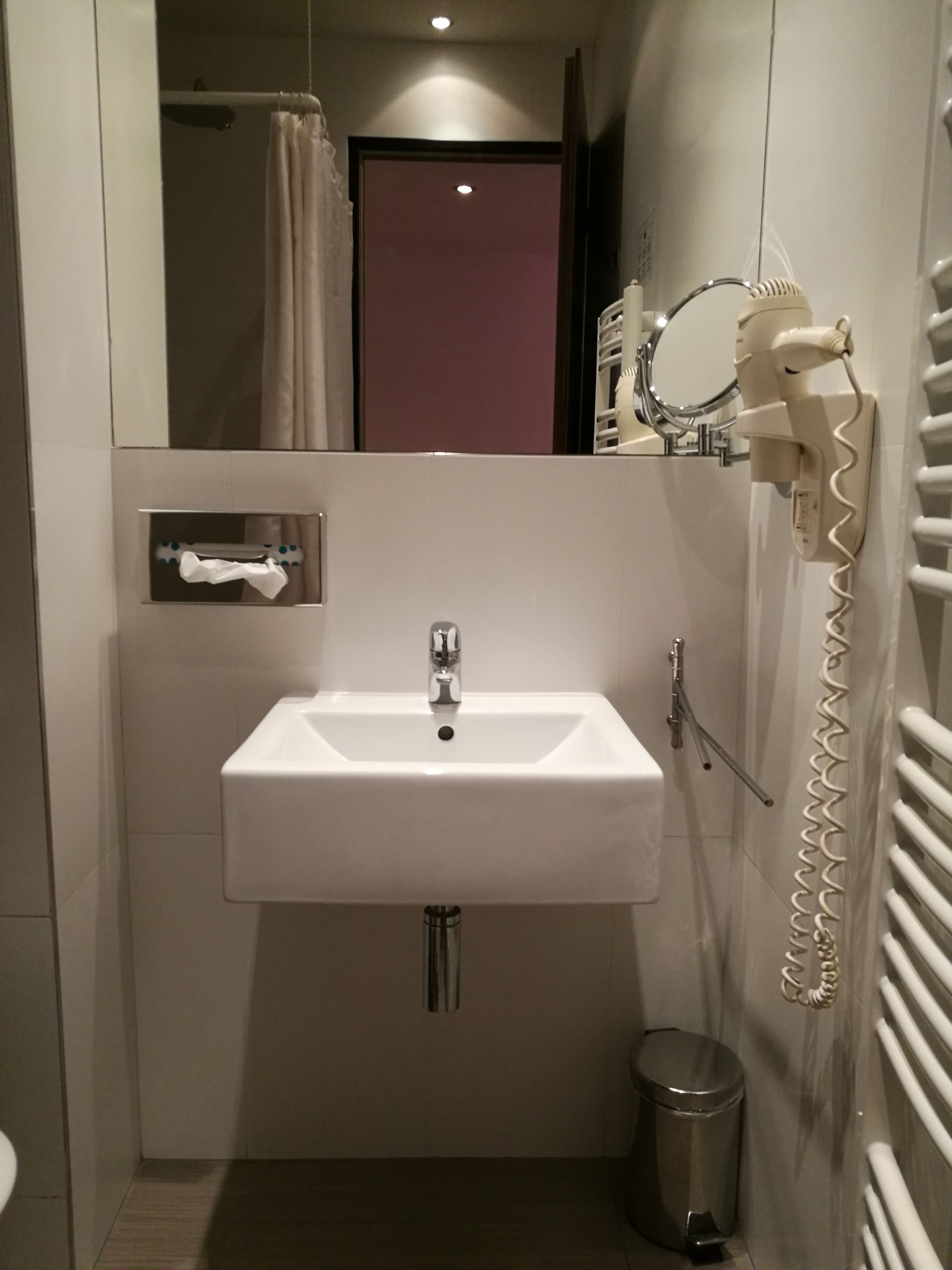 A compact bathroom with a white sink, a mirror, a hairdryer, and a towel rack.