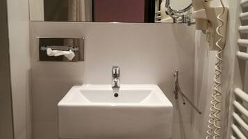 A compact bathroom with a white sink, a mirror, a hairdryer, and a towel rack.