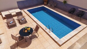 A rectangular swimming pool with a tiled deck, surrounded by lounge chairs and a table with a vase of flowers. - Hotel Dan Inn Barretos By Nacional Inn  (Barretos)